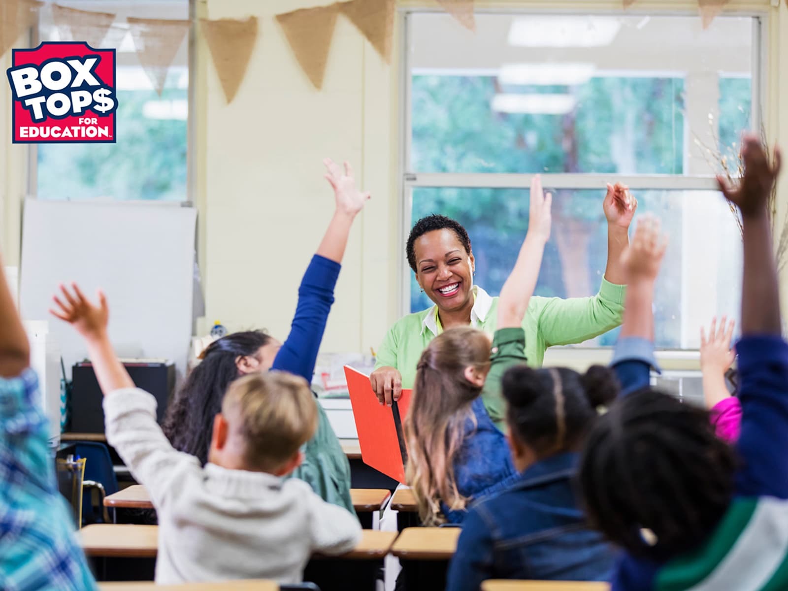 Teacher in a classroom of children raising their hands